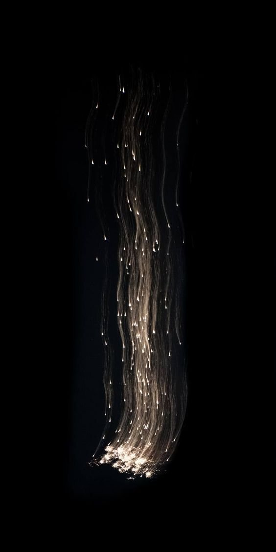 Long exposure of sparks of light falling in wavering lines through darkness
